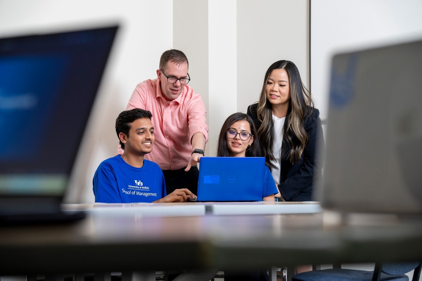Professors Michael Krupski and Cassie Nguyen (standing) with graduate students Abhishek Harihar and Kavita Pant who are seated in front of a laptop in the Projects Clinic space in Alfiero Center.