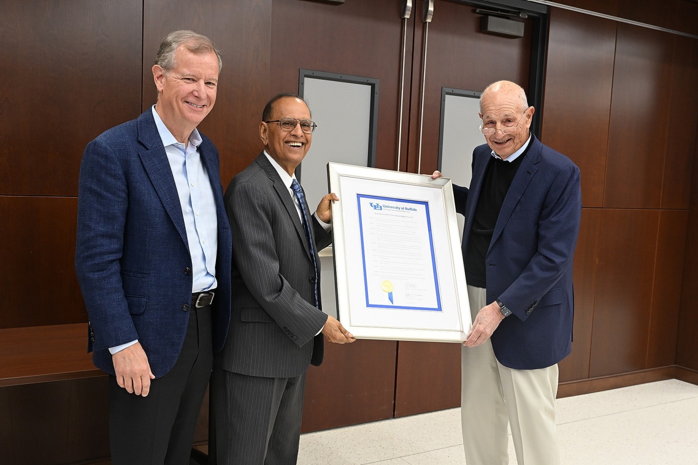 From left, Jeremy Jacobs Jr. and President Tripathi present a framed proclamation to Jeremy Jacobs Sr.