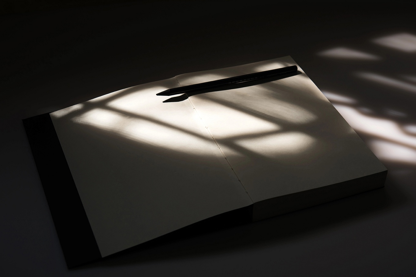 Concept of prisoners writing while incarcerated featuring a notebook and pencil with the shadow of prison bars falling across them. 