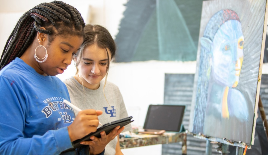 Two students look at a tablet in a painting classroom.. 