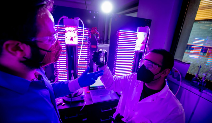 Two researchers look at an oject in a room with colorful lighted tubes. 