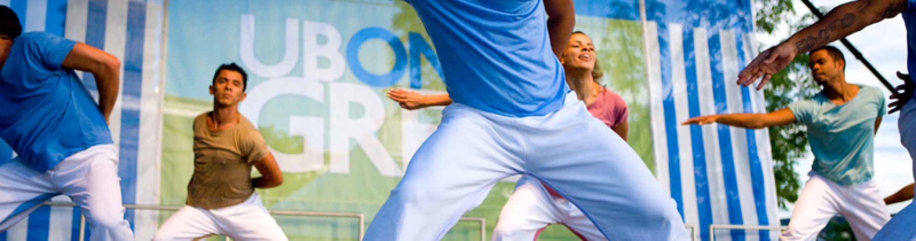 Two male dancers in blue gesture on stage at a UB on the Green outdoor event.